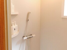 Un baño con ducha, dispensador de jabón y perchero.