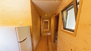 Un estrecho pasillo de madera con un refrigerador blanco a la izquierda y una ventana a la derecha.