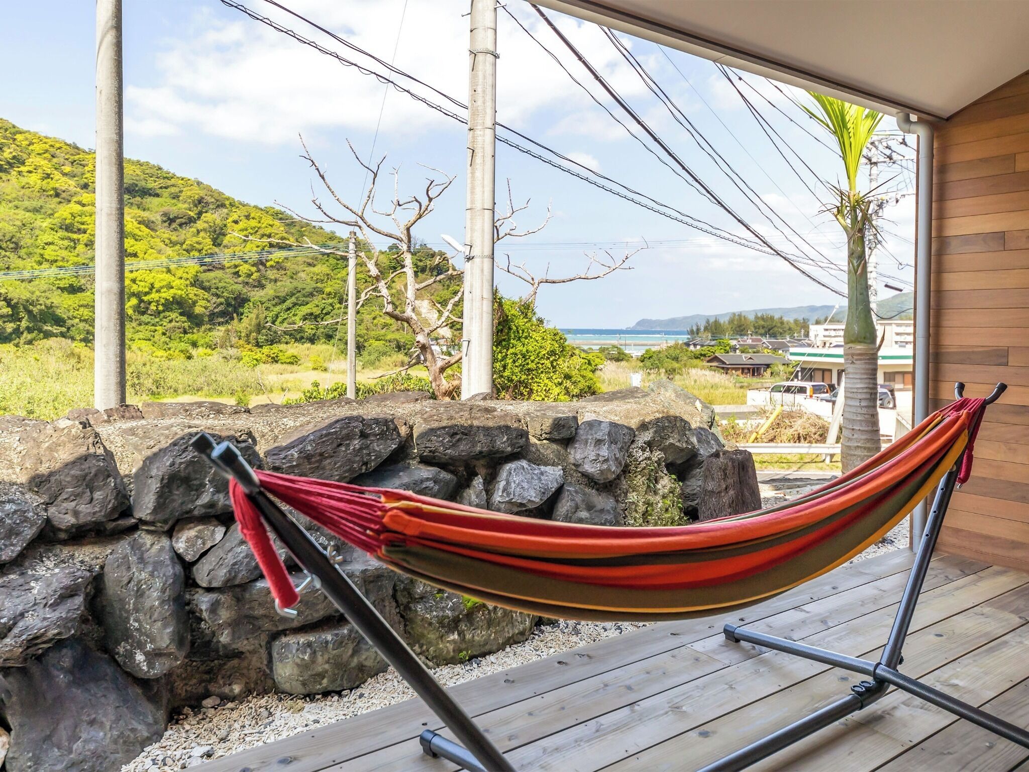 A hammock on a wooden deck with a view of a rocky landscape and a distant view of a town.