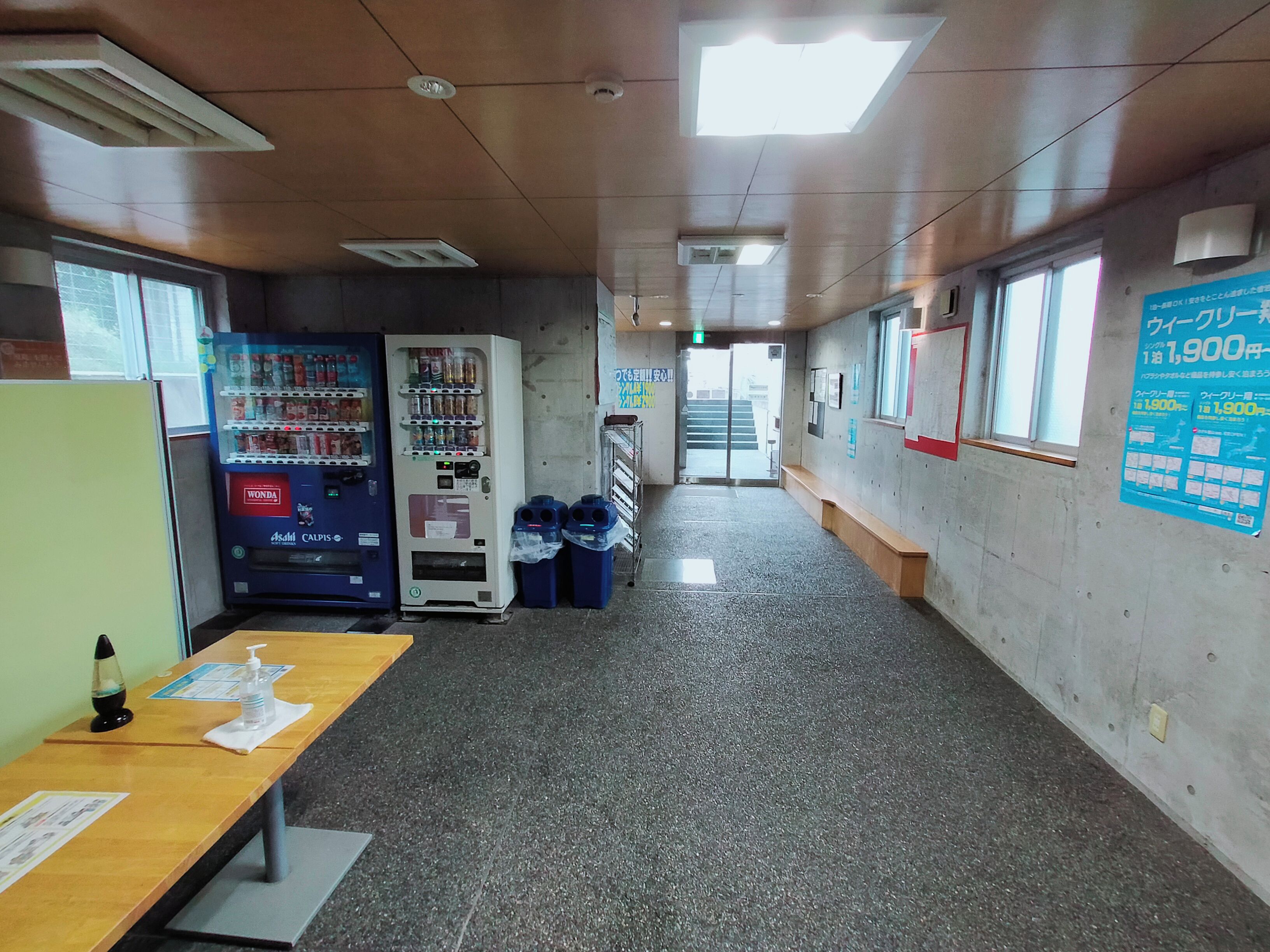 Un pasillo con máquinas expendedoras, una mesa con una botella y una servilleta, y un cartel en la pared.