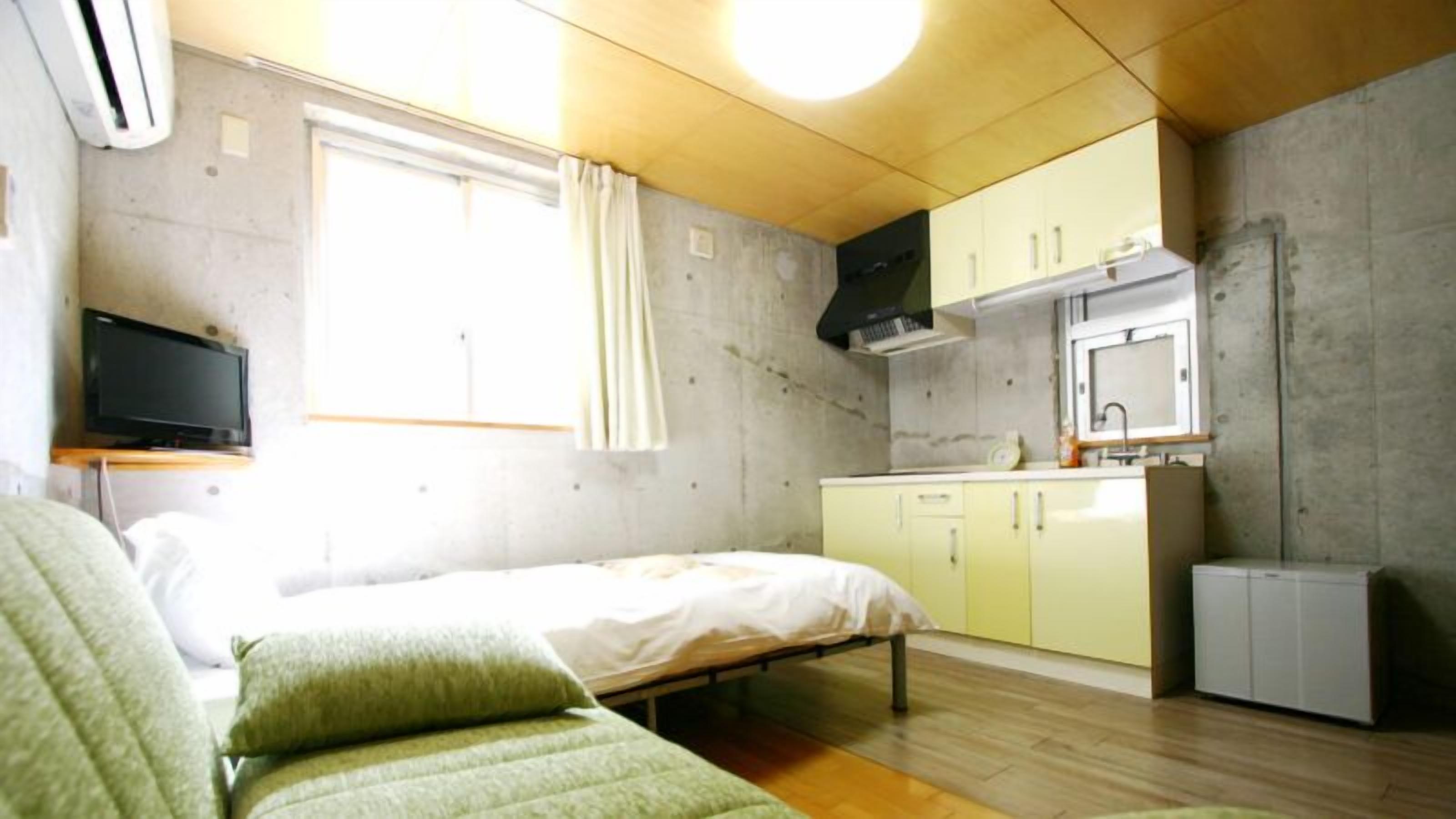 A compact room with a bed, a television, a kitchenette, and a window with curtains.