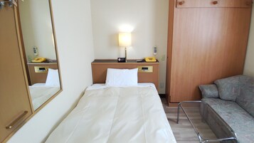 Habitación de hotel con cama, mesita de noche, lámpara y un pequeño rincón de descanso.