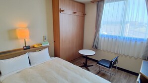 Habitación de hotel con cama, mesita de noche con lámpara, teléfono y una pequeña mesa redonda con silla.