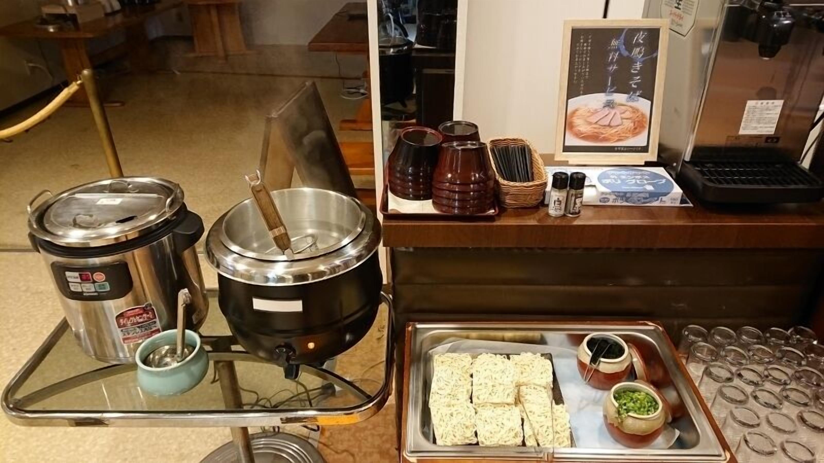 Montaje de bufé con una olla caliente, una bandeja de pan rebanado, salsas y una máquina de café.