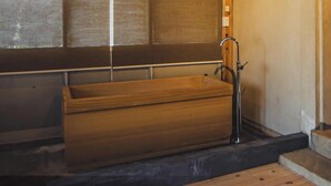 Une baignoire en bois dans une pièce dotée d’une fenêtre et d’un robinet en métal.