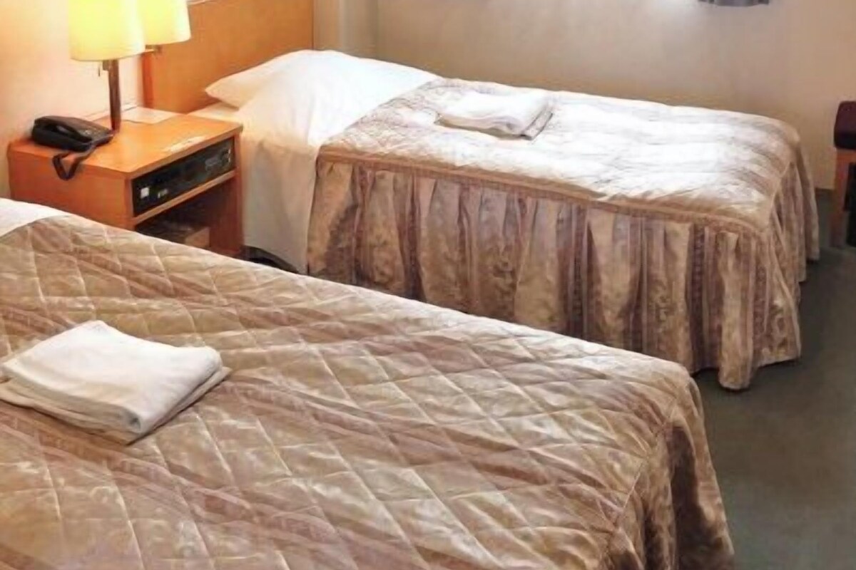 Une chambre d’hôtel avec deux lits, une table de chevet avec une lampe et une fenêtre avec des rideaux.