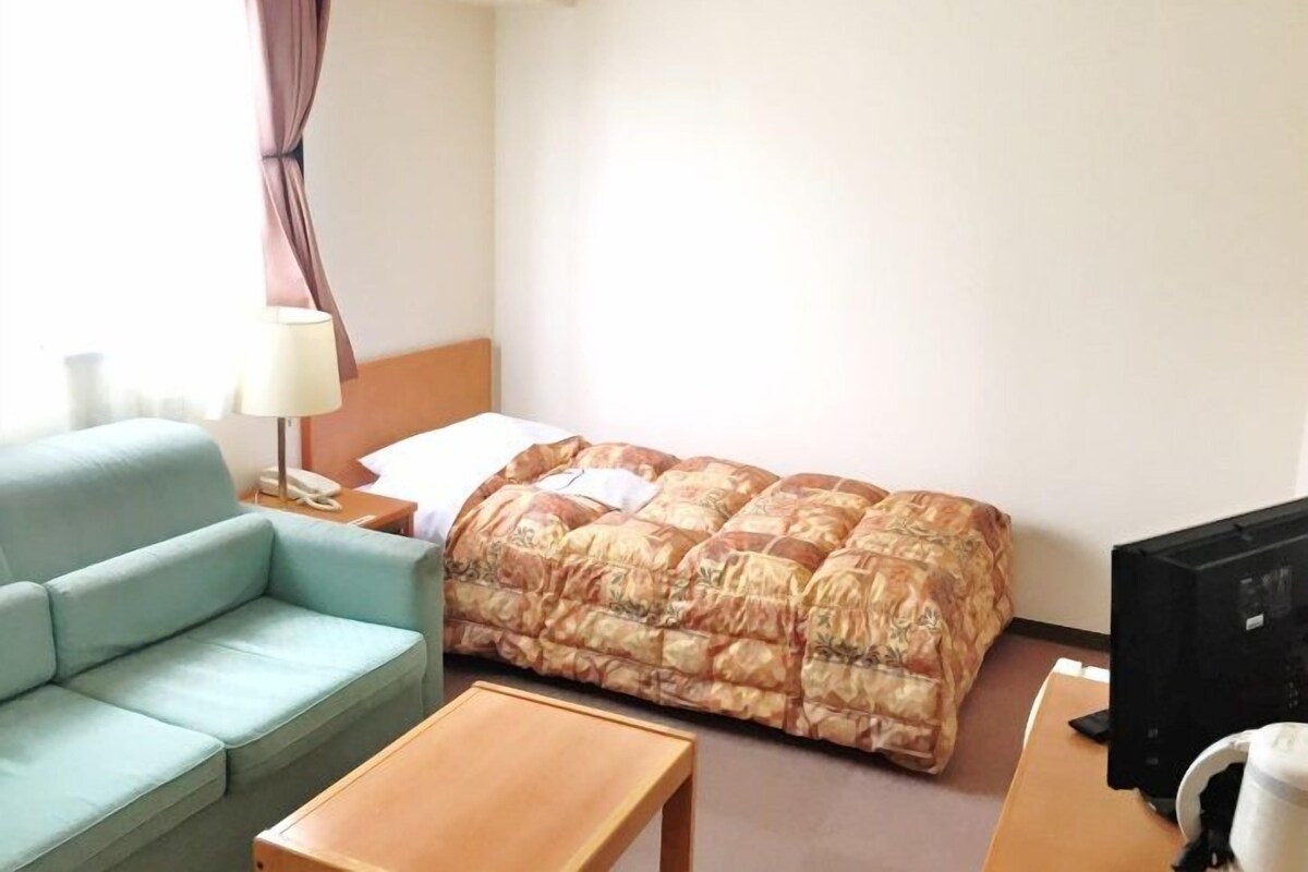 Une chambre d’hôtel avec un lit, un canapé, une petite table, une lampe et un téléviseur.