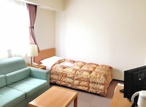 A hotel room with a bed, a light blue sofa, a wooden coffee table, a lamp, and a television.