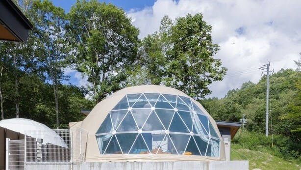 Una estructura geodèsica amb sostre transparent, envoltada d'arbres i una tanca.