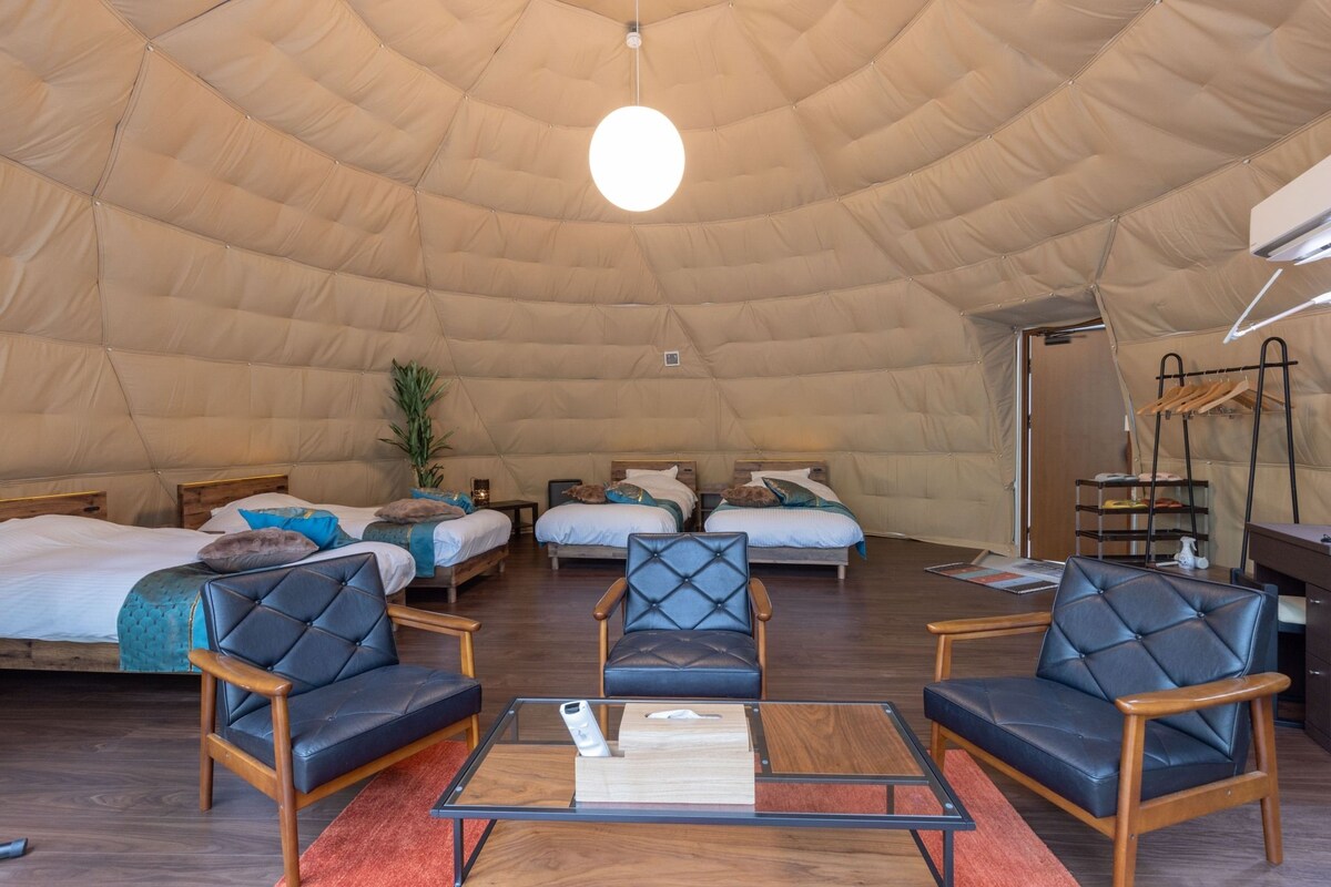 Een ruime tent met meerdere bedden, een gezellige zithoek en een hanglamp.
