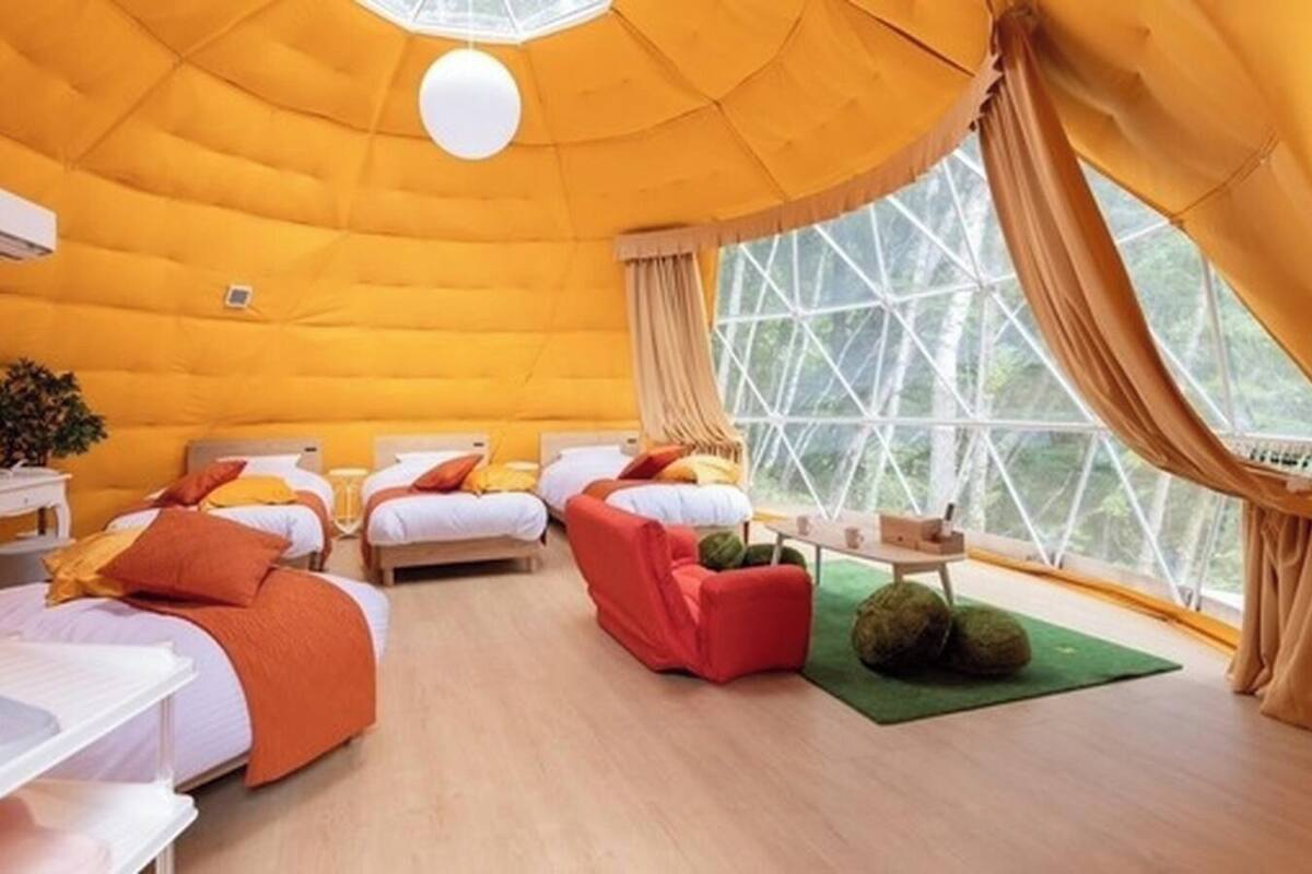 Una habitación acogedora con cuatro camas, una mesita pequeña y un ventanal amplio.