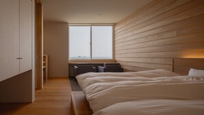 A modern bedroom with a large bed, a built-in bench, and a window with a view of the sea. - Hashimotoya (Himi)