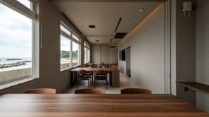 A modern interior with a long table, chairs, and a view of the sea. - Hashimotoya (Himi)