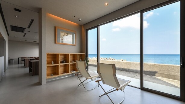 A modern interior with a large glass door leading to a beach view, wooden shelves, and a dining area. - Hashimotoya (Himi)