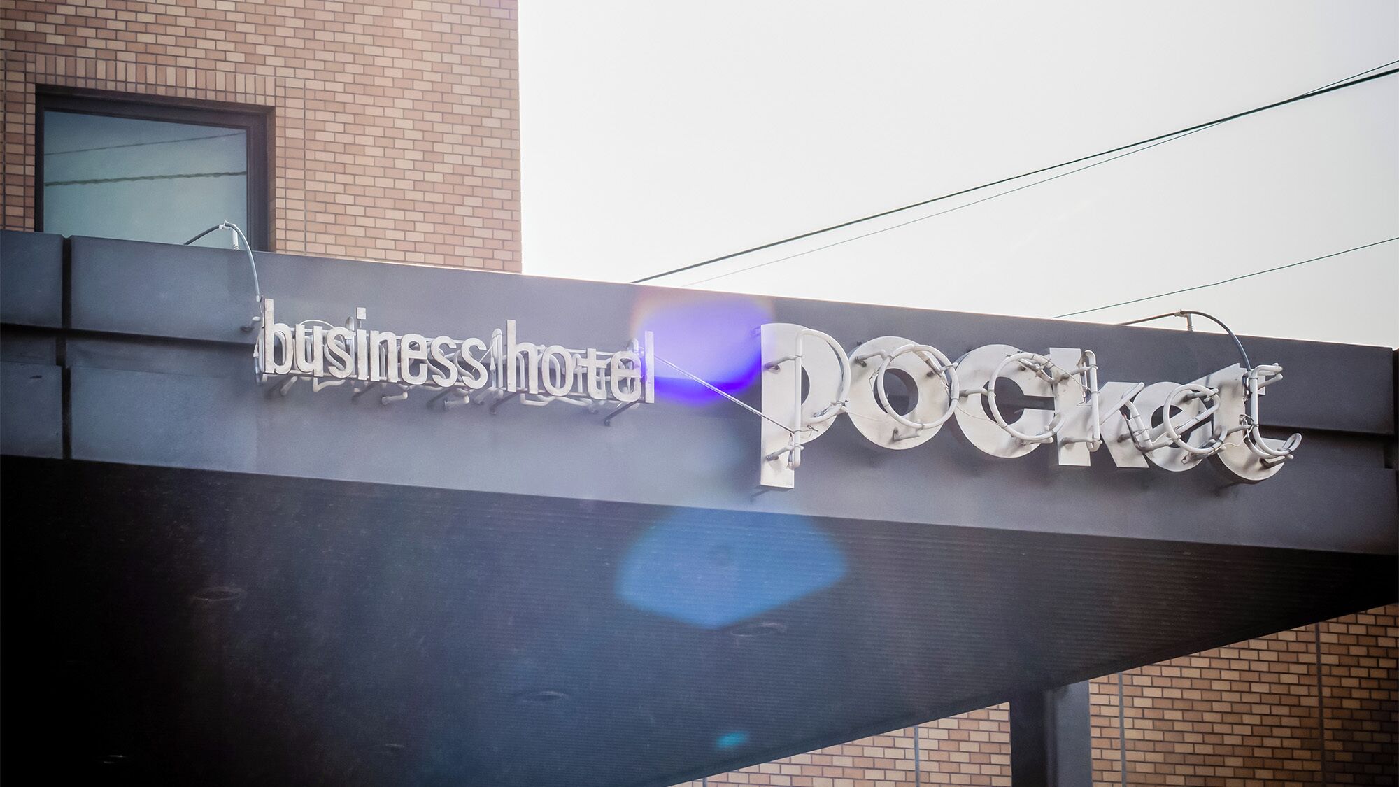 A sign for 'business hotel POCKET' with a modern design and a clear view of the building's brick facade.