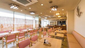 Uma sala de jantar ampla, com várias mesas e cadeiras, cozinha ao fundo e uma janela grande que ilumina o espaço com luz natural.