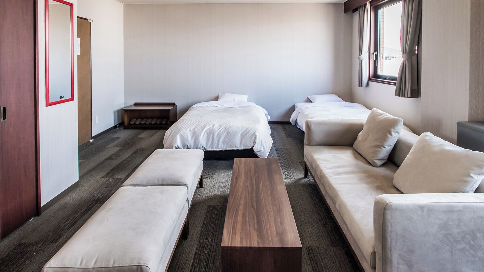 A hotel room with a large bed, two smaller beds, a sofa, a bench, and a wooden coffee table.
