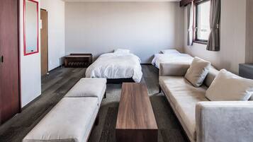 A hotel room with a large bed, two smaller beds, a sofa, a bench, and a wooden coffee table.