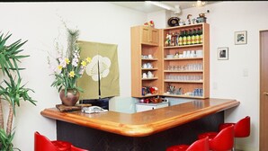 A kitchen with a wooden counter, red bar stools, a potted plant, and a shelf with bottles and dishes. - Kiryu Hotel Toseikan (Kiryu)