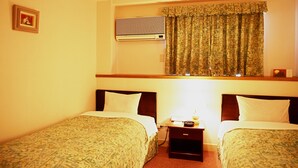 A hotel room with two single beds, a small bedside table with a lamp, an air conditioning unit, and a window with patterned curtains. - Kiryu Hotel Toseikan (Kiryu)