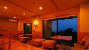 A spacious room with wooden flooring, a large window, and a seating area with tables and chairs. - Tsukiyado Rakku (Ito)