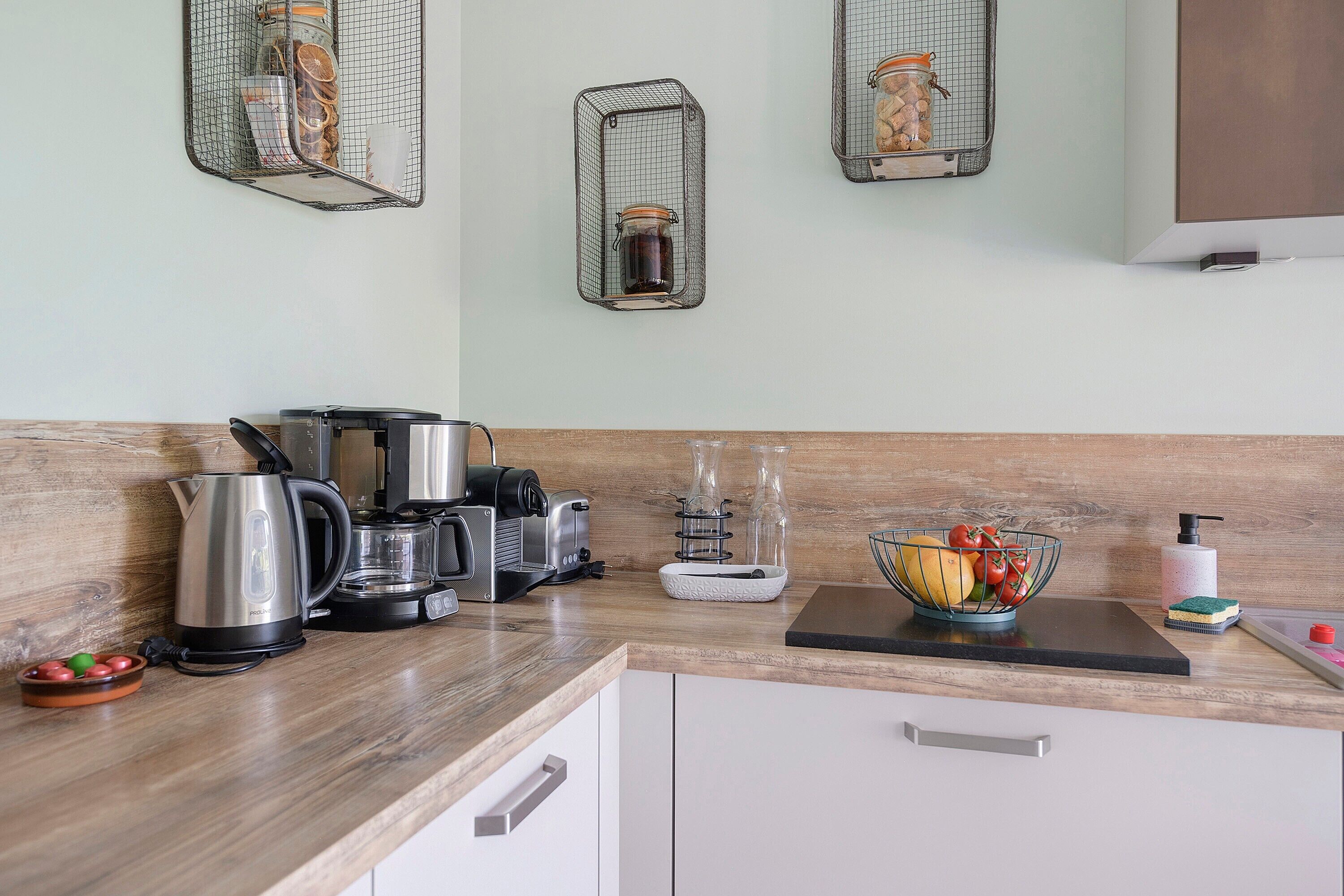 A kitchen with a coffee maker, kettle, blender, and a fruit bowl on the counter.