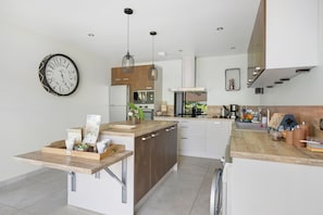 A modern kitchen with a central island, pendant lights, and a wall-mounted clock.