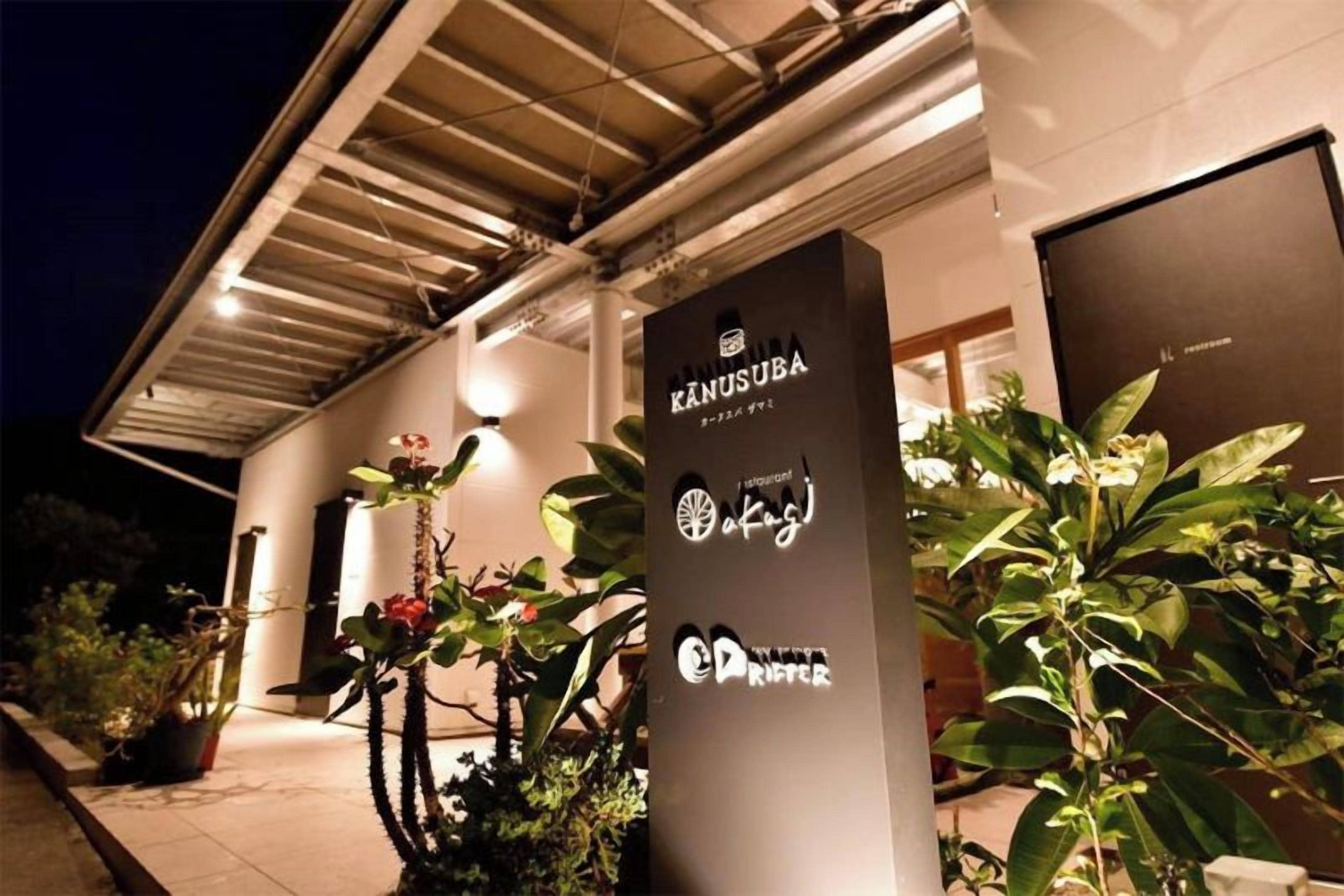 Un edificio con un cartel que dice 'KANUSUBA' y algunas plantas en la entrada.