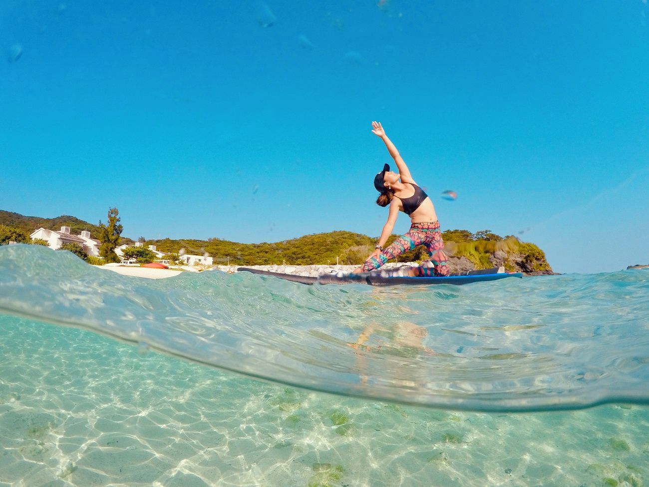 Una persona surfeando en un mar azul transparente con un pueblo costero al fondo.