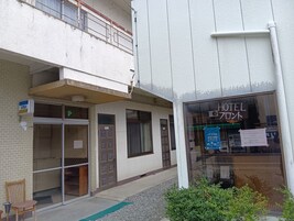 Entrada de hotel con un letrero de Visa, una puerta con el número 102 y una ventana que muestra el cartel de 'Hotel 700'.