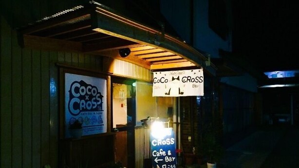 Vue nocturne d’un bâtiment sur lequel on peut voir une enseigne indiquant « Coco Cross Cafe & Bar ».