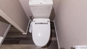 Des toilettes blanches, équipées d’un siège-bidet, dans une petite salle de bain étroite au sol en bois.