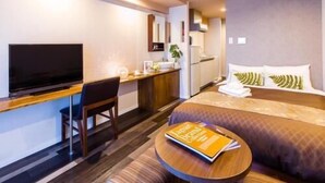 Une chambre d’hôtel avec un lit, un bureau, une télévision et une petite table ronde sur laquelle se trouve un livre.