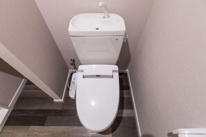 A modern toilet with a control panel, a bidet attachment, and a wall-mounted bidet seat. - Mr.kinjo in Shanti Van Tsubogawa Station (Naha)