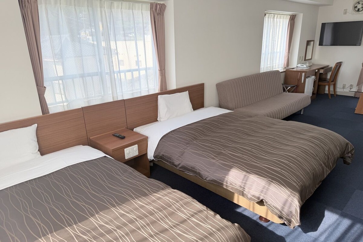 A hotel room with two beds, a desk, and a TV.