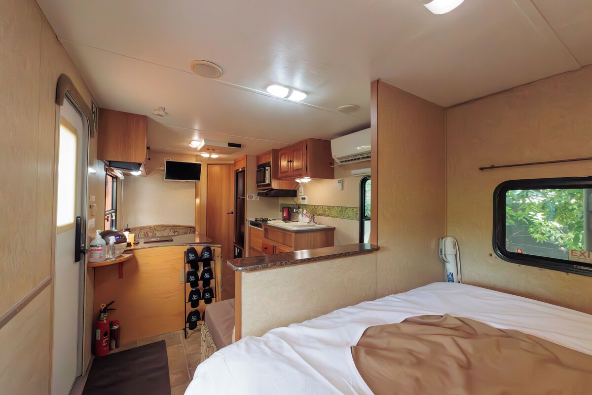 Interior compacto de una caravana con kitchenette, una cama y una ventana.