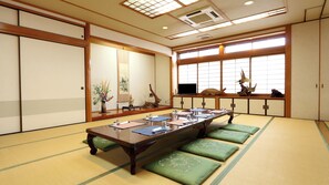A traditional Japanese room with tatami flooring, a low table with cushions, sliding doors, and a large window with a view. - Ryori Ryokan Marumo (Takashima)