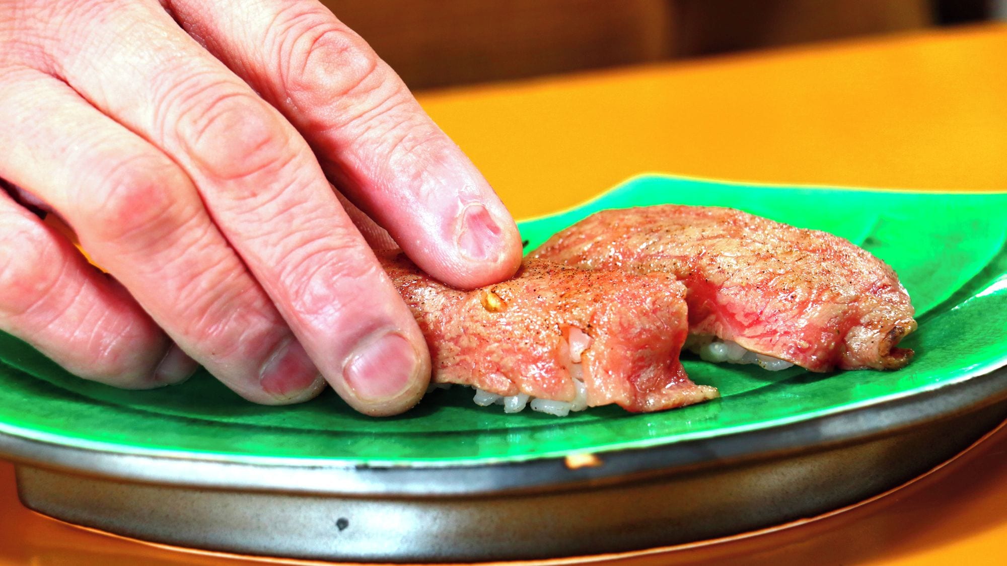 A hand holding a piece of food on a green plate.