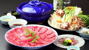 A table with various food items including a blue pot, bowls of soy sauce, and plates of meat and vegetables. - Ryori Ryokan Marumo (Takashima)