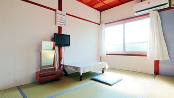 Una habitación con suelo de tatami, una cama, un televisor, un calendario y una ventana con cortinas.