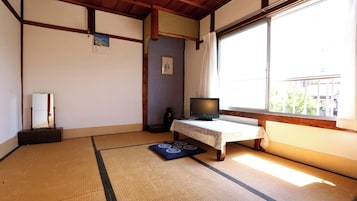 Una habitación japonesa tradicional con suelo de tatami, un televisor sobre una mesa baja y una ventana con vistas al exterior.