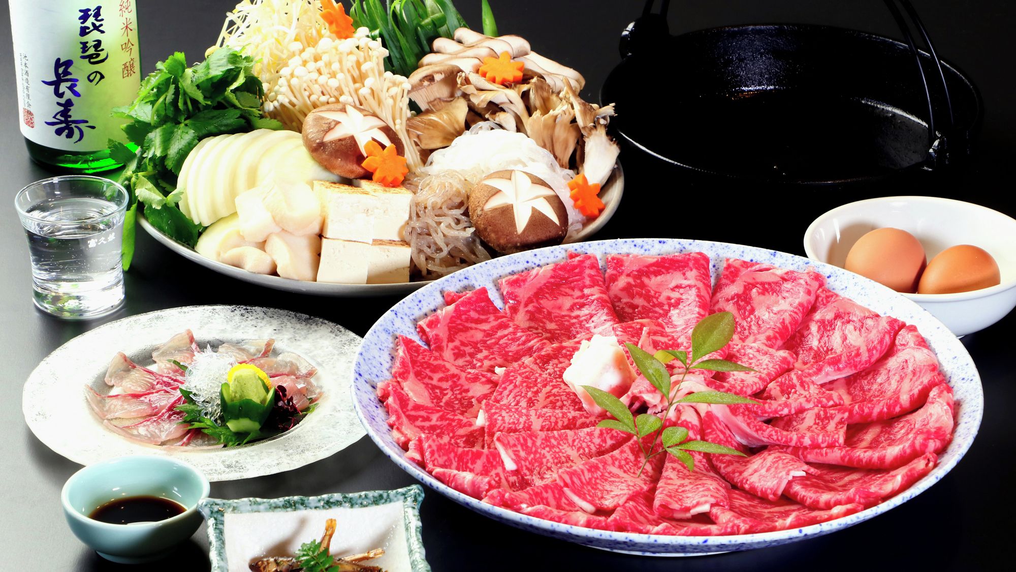 A variety of Japanese dishes including sashimi, vegetables, and a hot pot.
