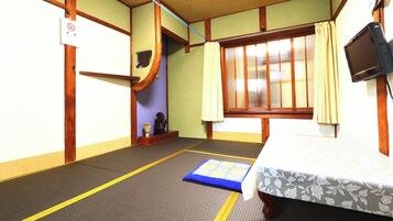 Una habitación japonesa tradicional con suelo de tatami, futón, televisor y puerta corredera.