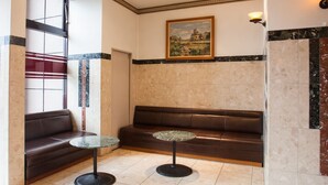 A lobby with a brown leather sofa, two glass-top tables, and a painting on the wall. - Hotel New Global (Isahaya)