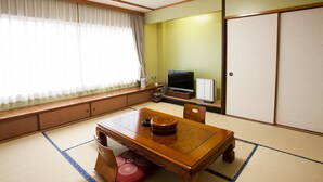 A traditional Japanese room with tatami flooring, a low wooden table, a TV, and sliding doors. - Hotel New Global (Isahaya)
