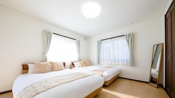 A bedroom with two beds, a wooden floor, and a large mirror on the wall. - Fuji Viewest Villa Rakuwa (Fujikawaguchiko)