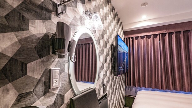 A modern hotel room with a geometric-patterned wall, a large mirror, a flat-screen TV, a bed, and a small desk area. - Hotel Prism (Nagoya)