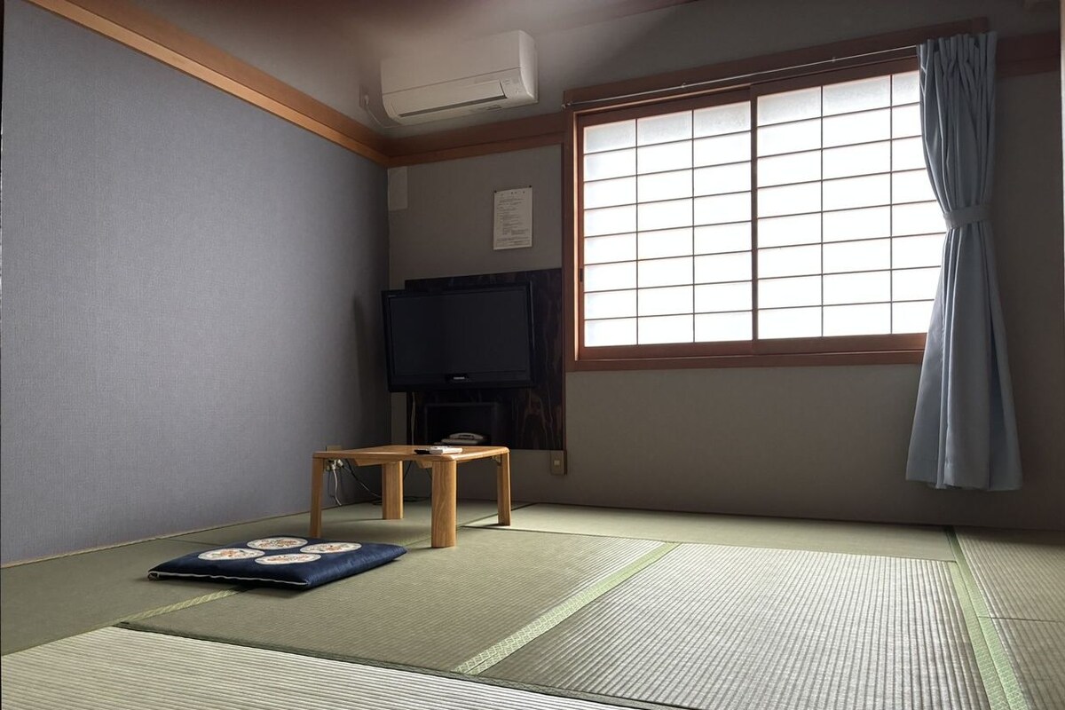 A traditional Japanese room with tatami flooring, a television, a small wooden table, and a futon.