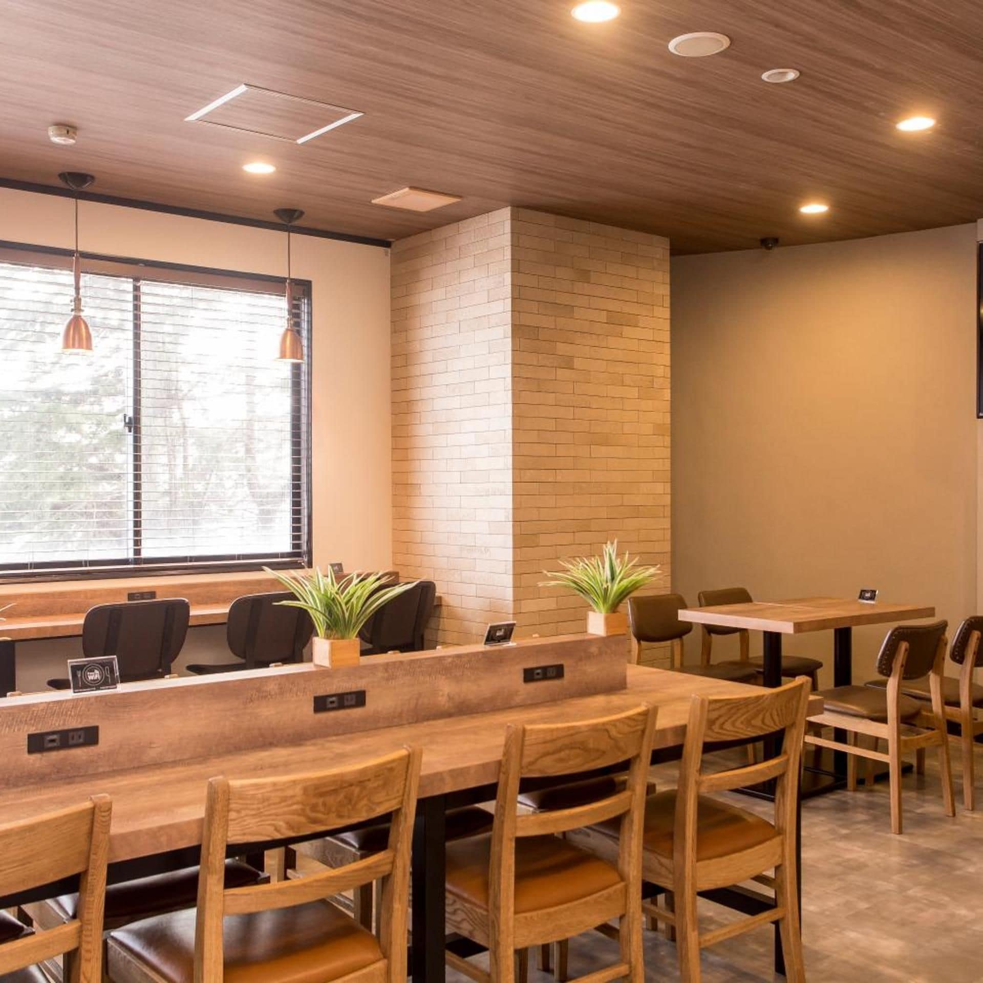 A modern interior with wooden tables and chairs, a brick accent wall, and pendant lighting.