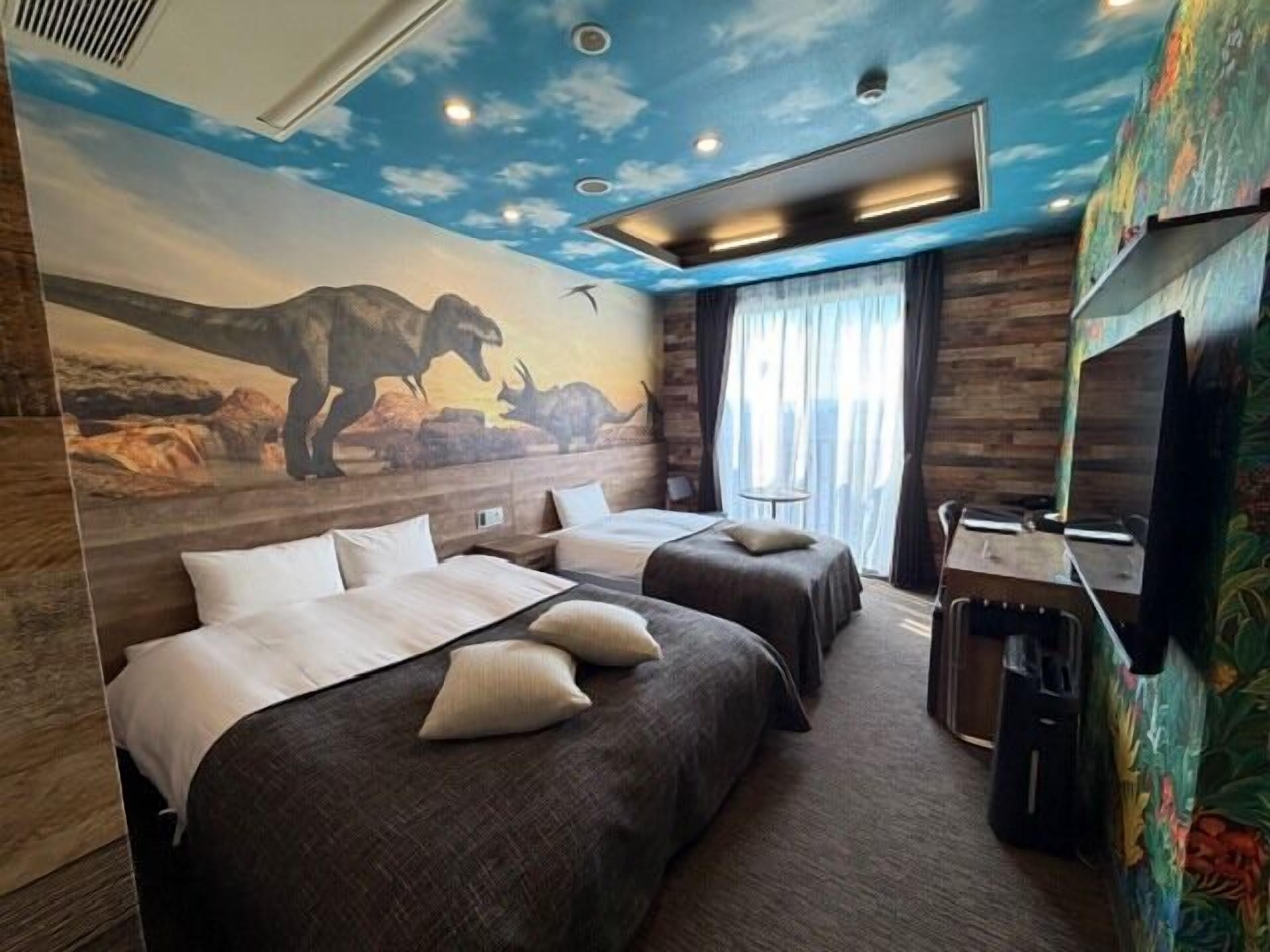 Una habitación con dos camas, televisión y un mural de dinosaurios.